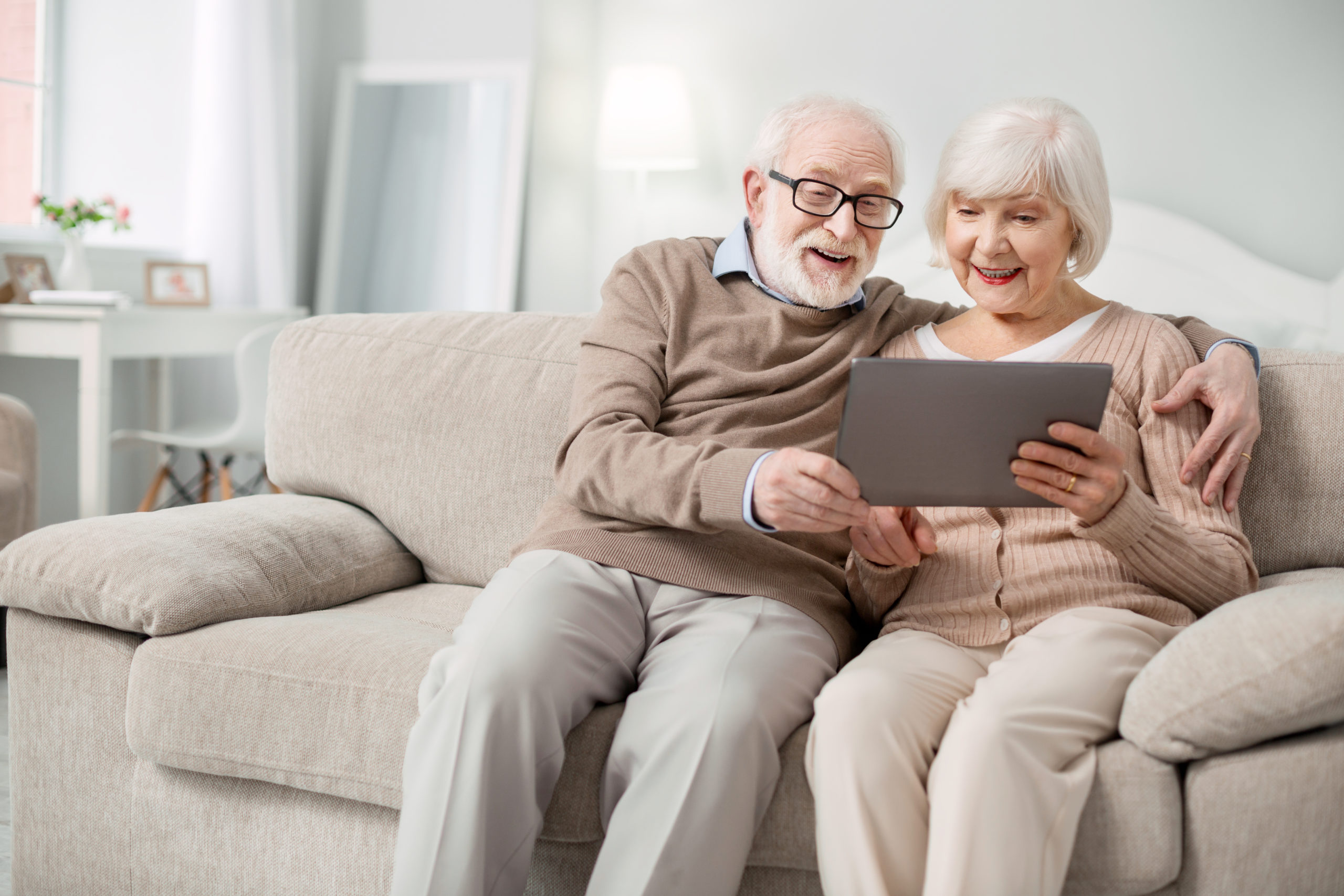 Modern device. Joyful aged people smiling while looking at the tablet screen